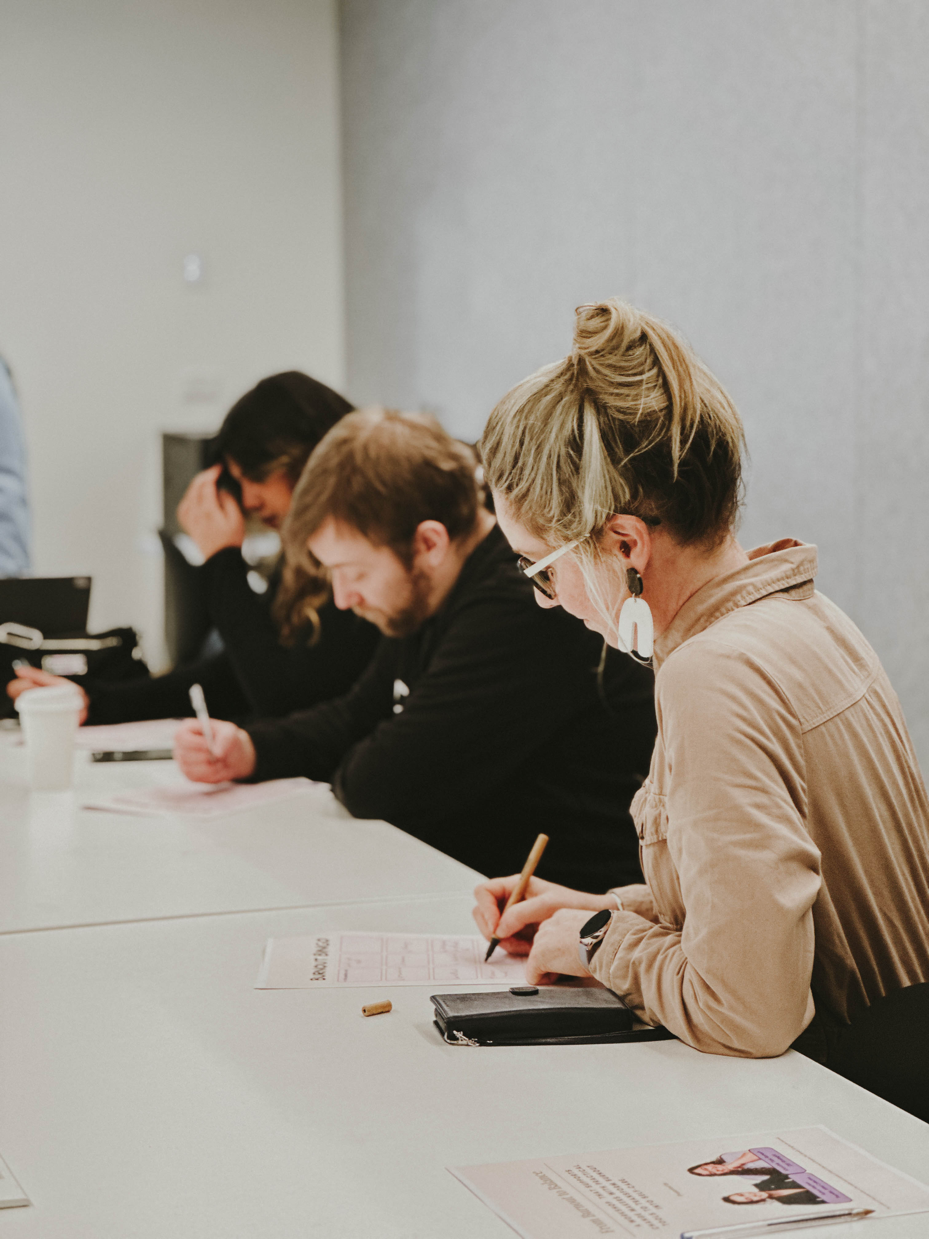 Workshop participants sit at a table, writing and reflecting on worksheets during a burnout and wellbeing session.